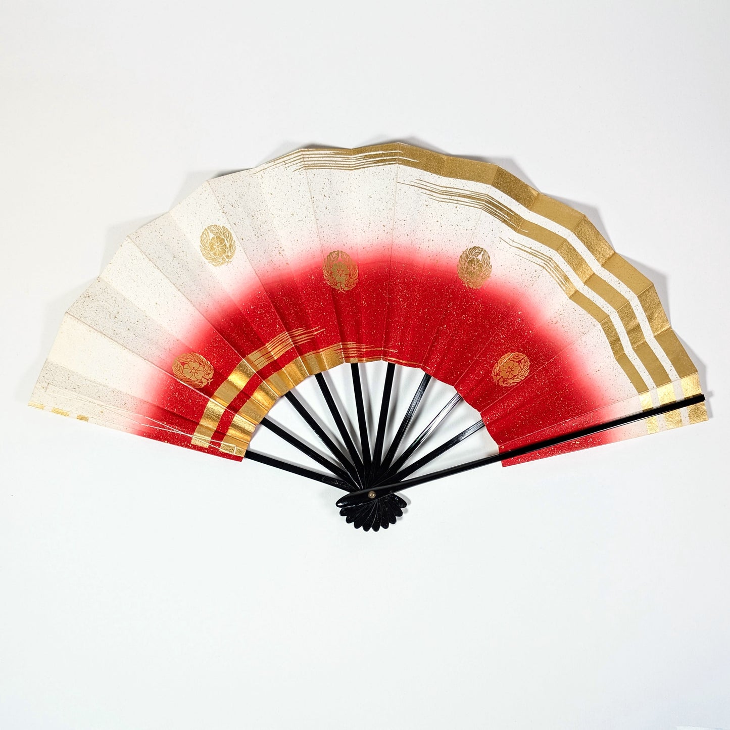 Vue d’ensemble d’un sensu japonais (éventail pliable) ouvert, avec ses motifs rouges, dorures graphiques et kamon stylisés, typiques des objets décoratifs nippons.