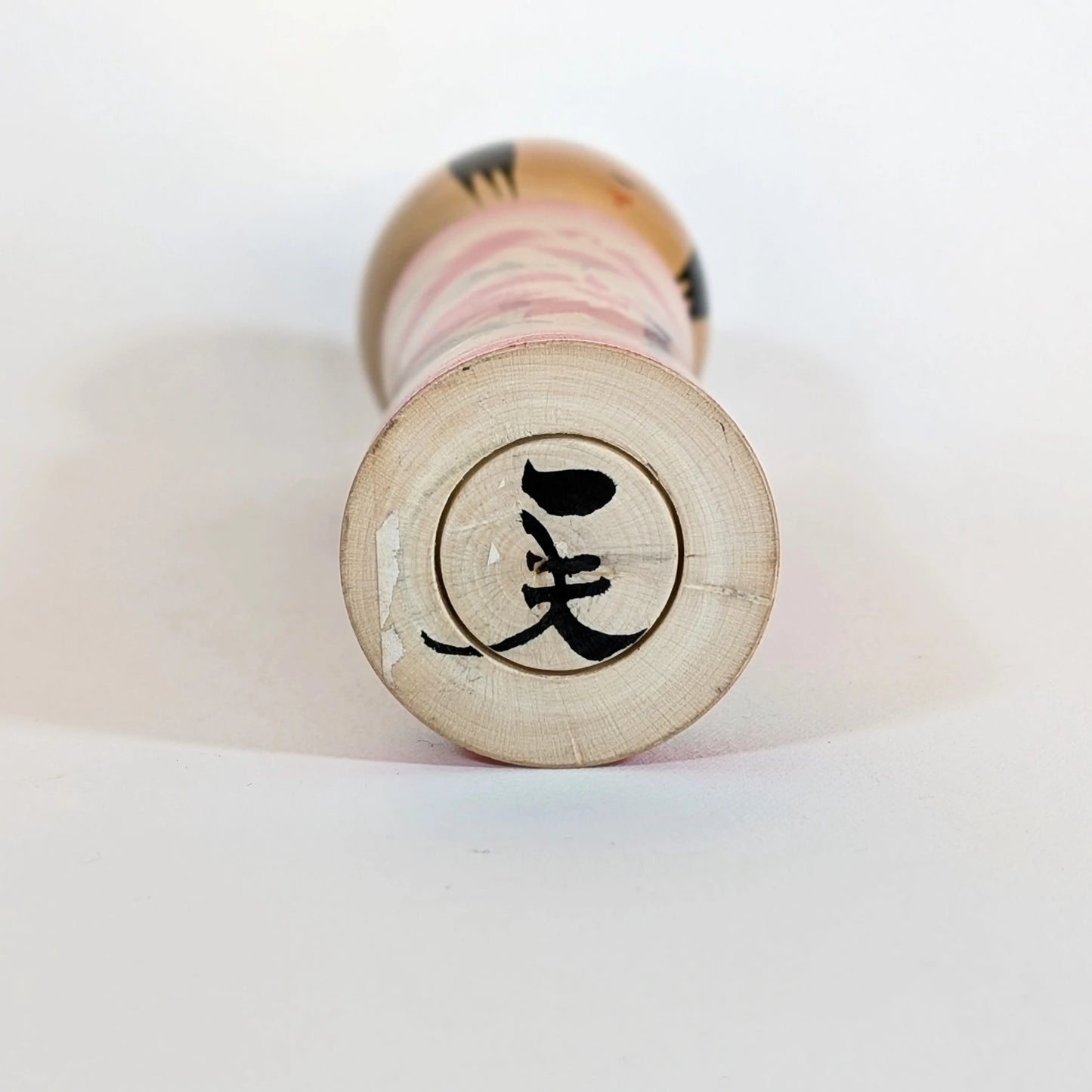 Signature calligraphiée sous la base d’une kokeshi Naruko de l’artisan Sato Kazuo.
