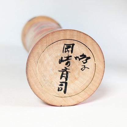 Signature 岡崎斉司 sous la base d’une kokeshi Naruko d’Okazaki Seishi, artisan japonais de la tradition des kokeshi du Tohoku.