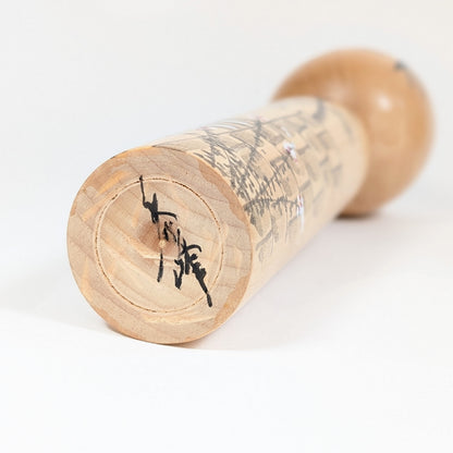 Signature de l’artisan Shūhō 秀峰 sous la base de la kokeshi japonaise en bois, vue rapprochée.