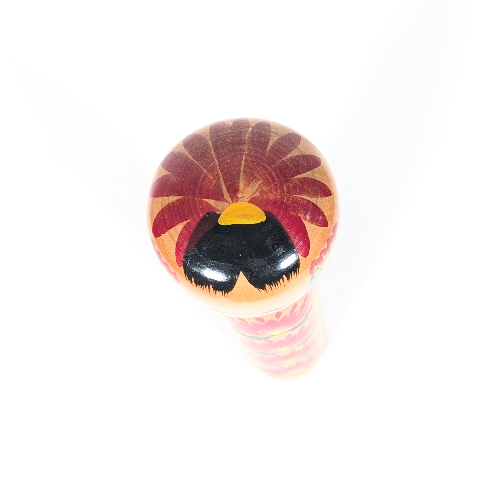 Vue du sommet de la tête d’une kokeshi shingata, décor kiku rouge, cheveux noirs brillants et jolie touche jaune peinte.