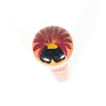 Vue du sommet de la tête d’une kokeshi shingata, décor kiku rouge, cheveux noirs brillants et jolie touche jaune peinte.