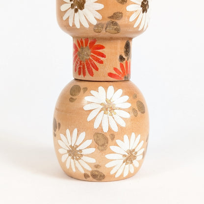 Décor floral d’une sosaku kokeshi Ishida Tomio avec fleurs orange, chrysanthèmes blancs et touches dorées.