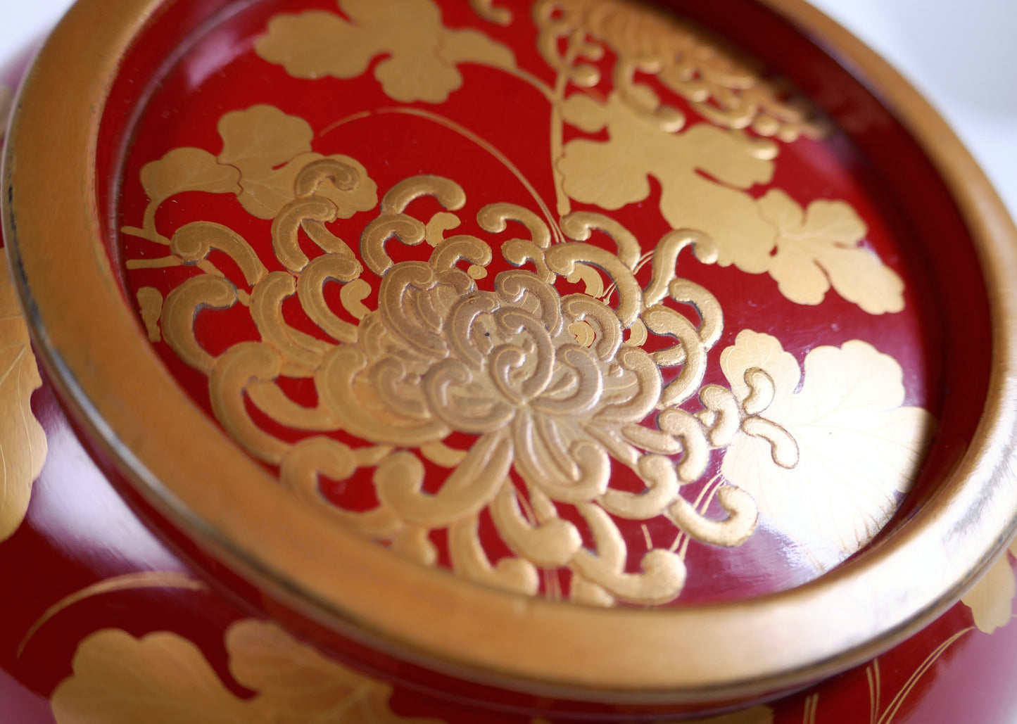 Gros plan d’un chrysanthème en taka-maki-e doré en relief sur le couvercle d’un bol japonais en laque urushi.