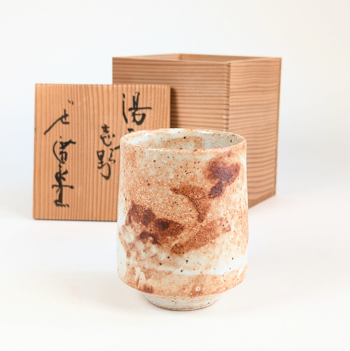 Yunomi, tasse à thé japonaise Shino de l'atelier Hironaga-gama, glaçure orangée et brune, devant son coffret tomobako en bois.