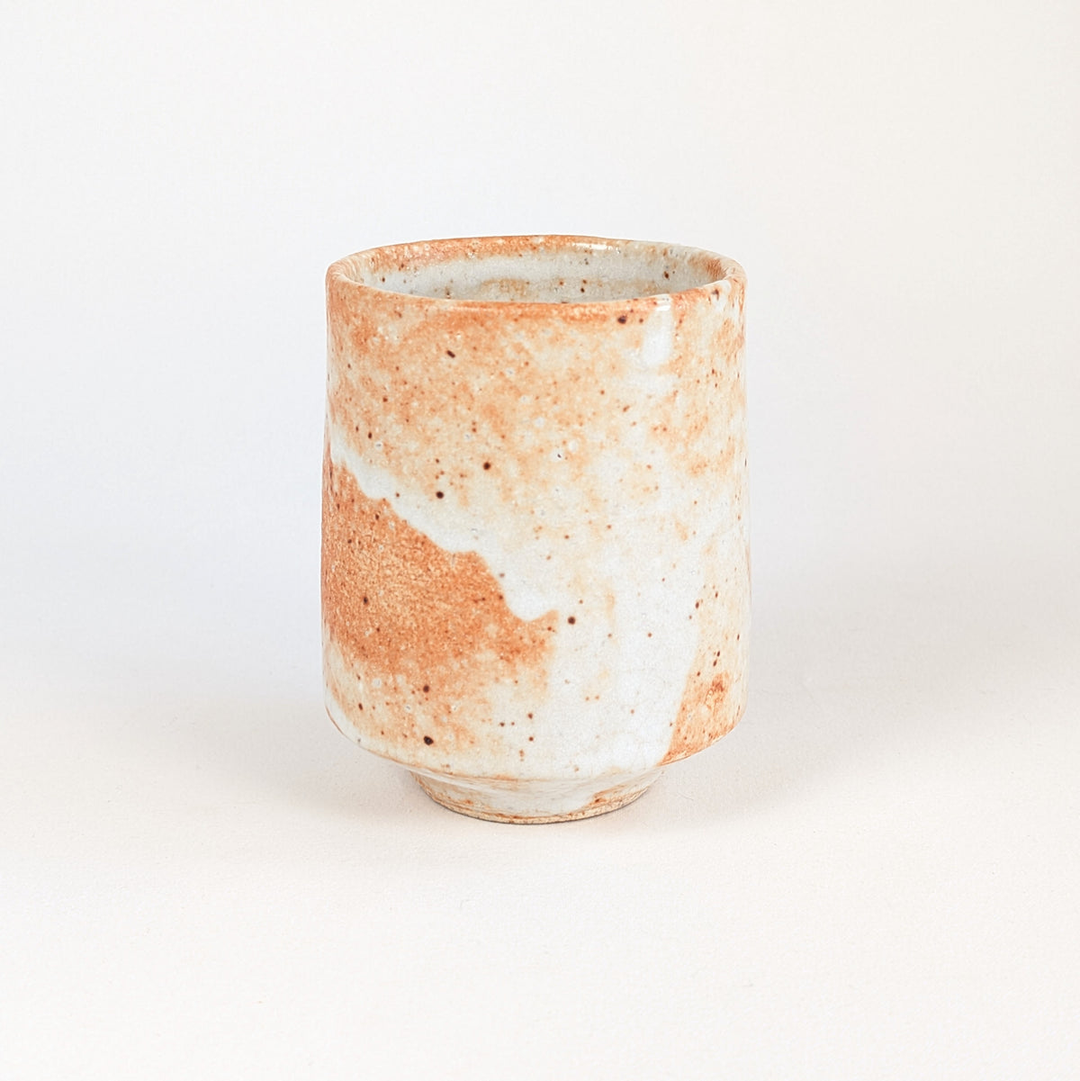 Vue latérale d'une tasse à thé japonaise en grès émaillé Shino, avec larges plages orange saumon et blanc crème.