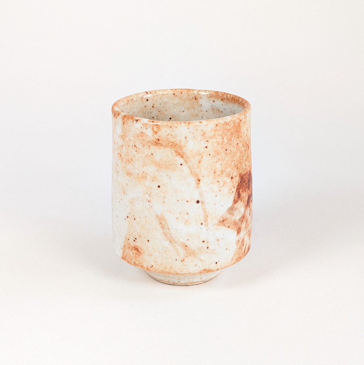 Face claire d'une tasse japonaise sans anse en grès Shino, glaçure blanc ivoire mouchetée de nuances orangées.