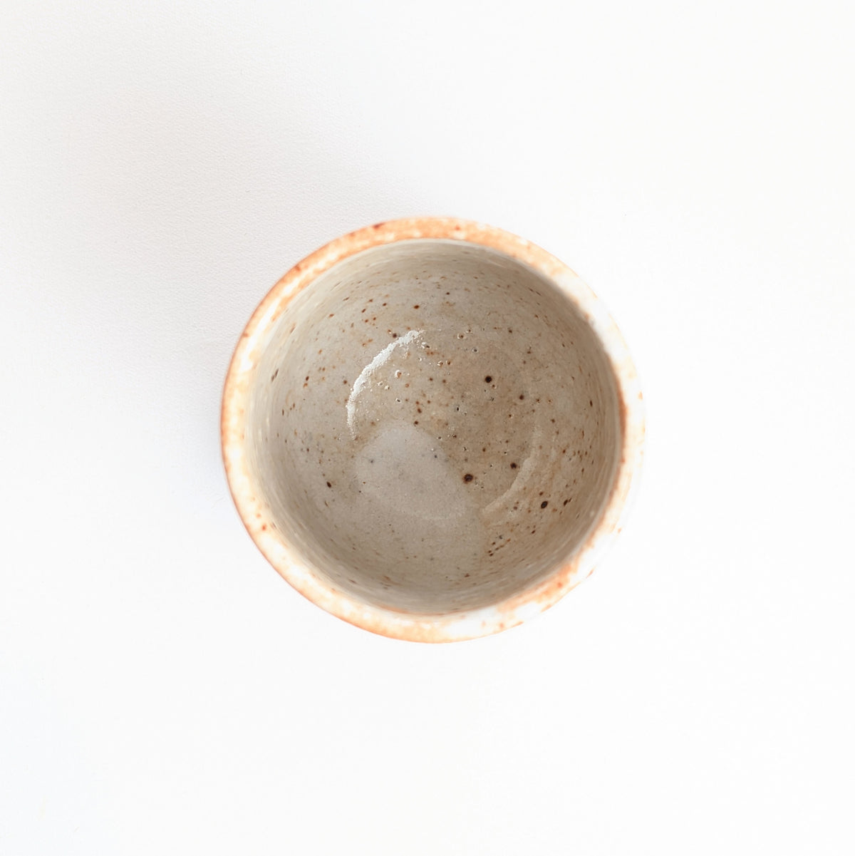 Vue plongeante dans une tasse yunomi japonaise, intérieur émaillé blanc crème moucheté de petits points bruns.