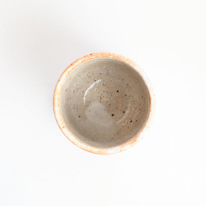 Vue plongeante dans une tasse yunomi japonaise, intérieur émaillé blanc crème moucheté de petits points bruns.