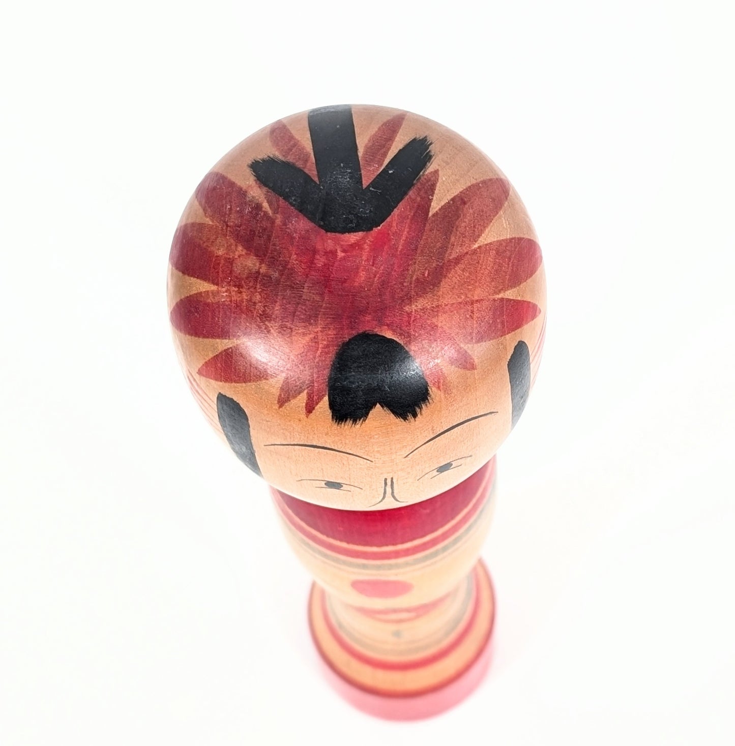 Vue du dessus de la tête arrondie d’une kokeshi Zao Takayu avec chevelure peinte à la main