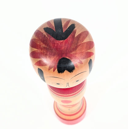 Vue du dessus de la tête arrondie d’une kokeshi Zao Takayu avec chevelure peinte à la main