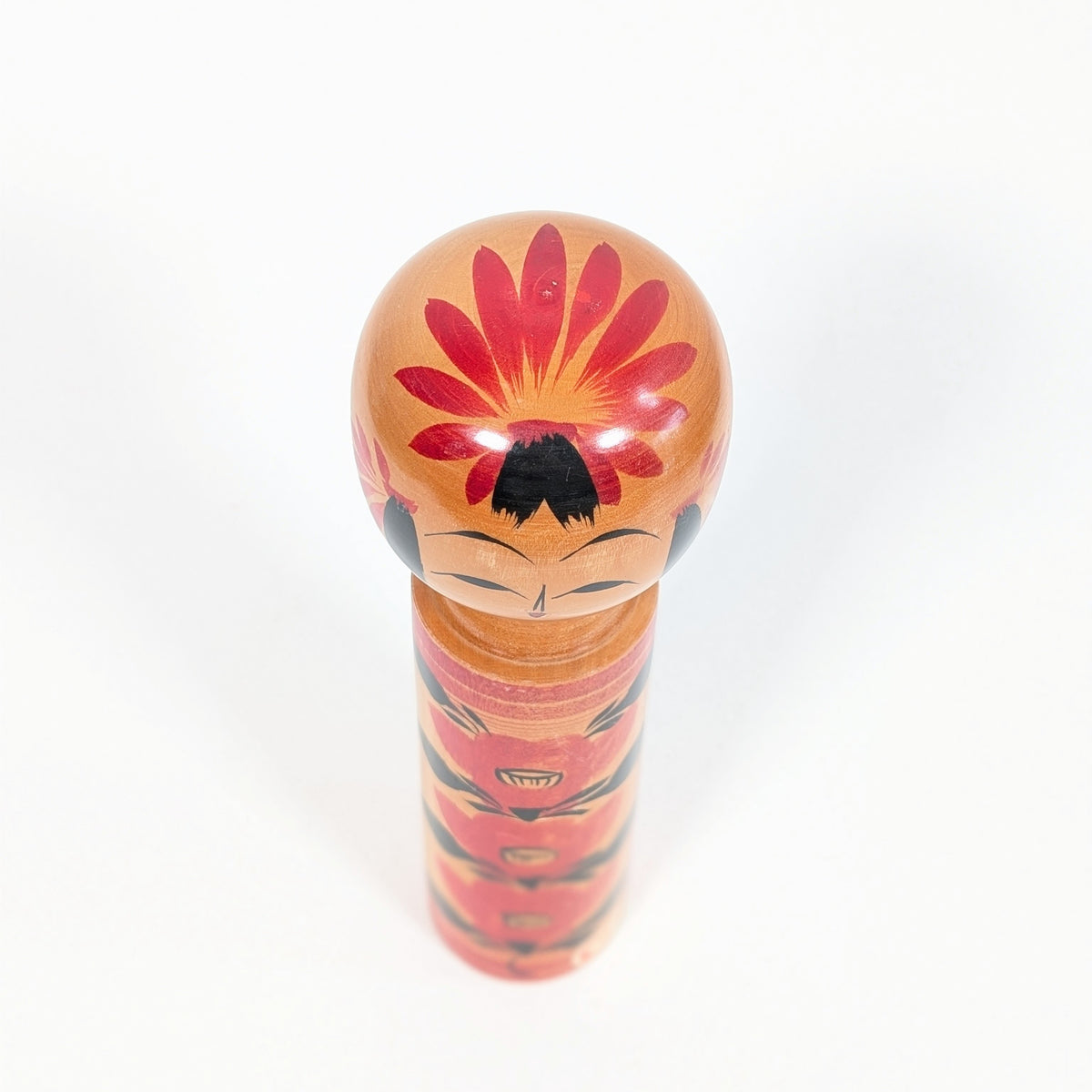 Vue du dessus d’une tête de kokeshi shingata décorée d’un grand camélia japonais tsubaki rouge