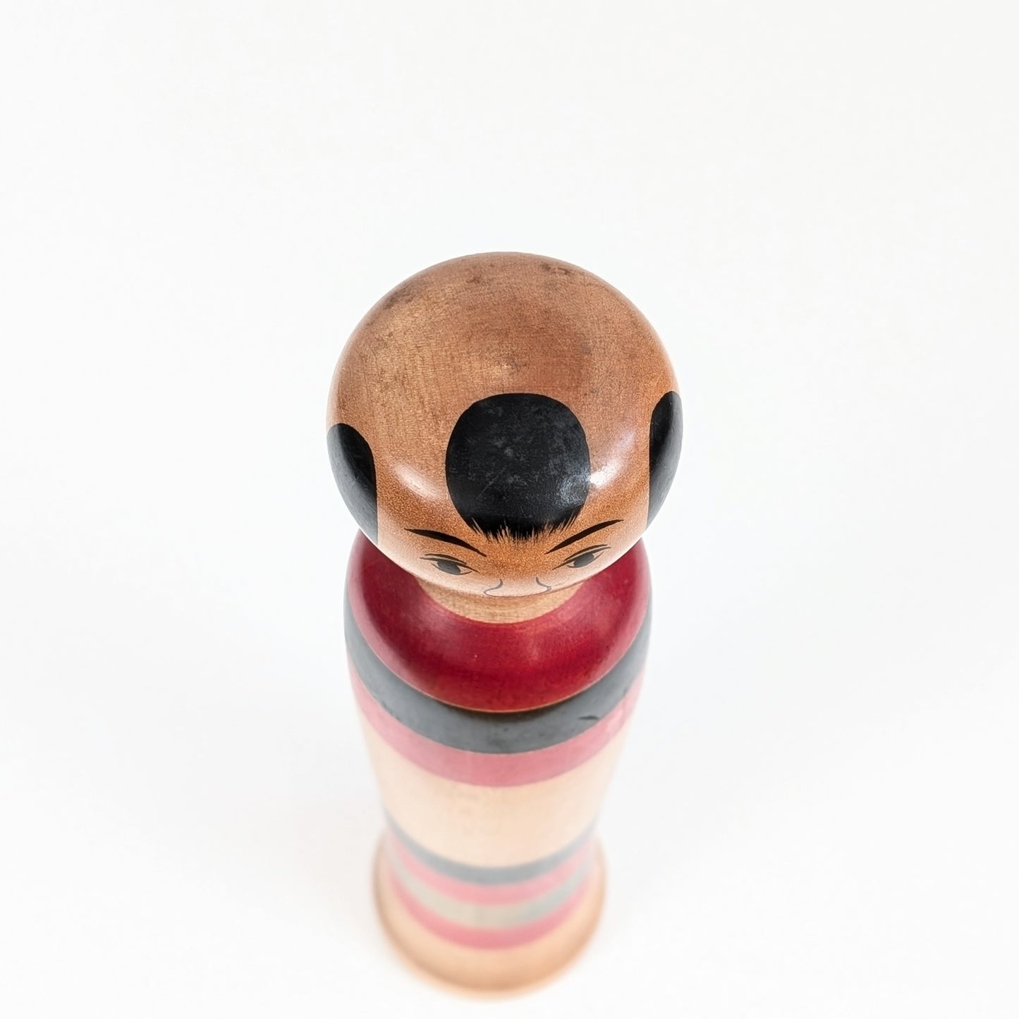 Vue plongeante de la tête d’une kokeshi Kijiyama de Satō Hideichi avec coiffure noire et traits du visage peints à la main