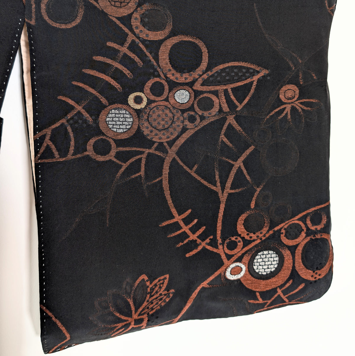 Détail d'une manche de haori en soie japonaise, avec motifs floraux abstraits, cercles géométriques et fils argentés sur fond noir cuivré.