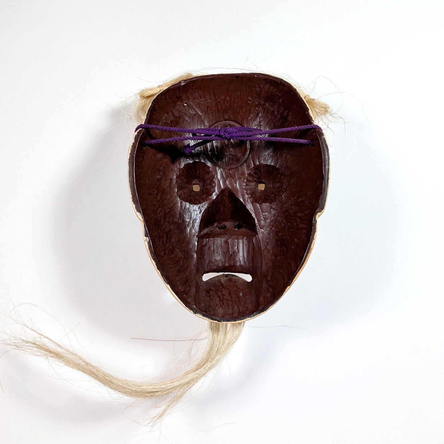 Intérieur d’un masque Nô japonais avec texture bois sculpté et fixation en corde violette, usage scénique traditionnel.