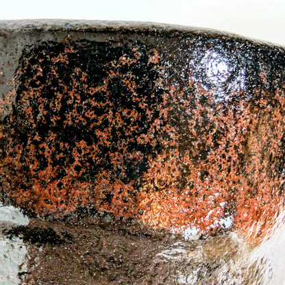 Détail de la glaçure d’un chawan en kuro raku signé Sasaki Shoraku, montrant la texture et les nuances rougeâtres du raku noir.