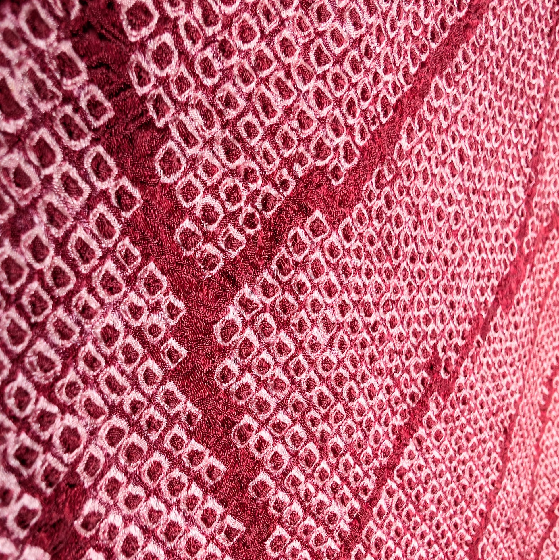 Texture shibori japonais en gros plan : soie rose fuchsia avec motif feuillage, teinture artisanale traditionnelle.
