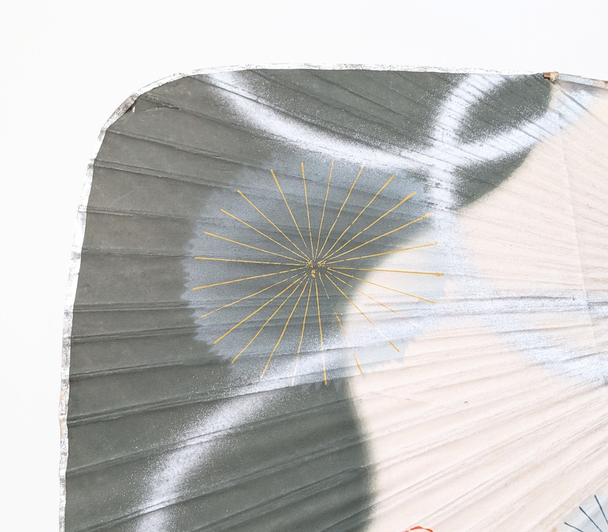 Gros plan d’un motif de feu d’artifice hanabi doré sur le décor vert argenté d’un uchiwa japonais.