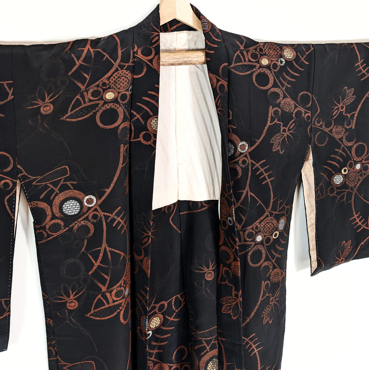 Vue rapprochée du col d'une veste kimono japonaise en soie noire, décorée de rinceaux végétaux cuivrés et de cercles aux reflets métalliques.