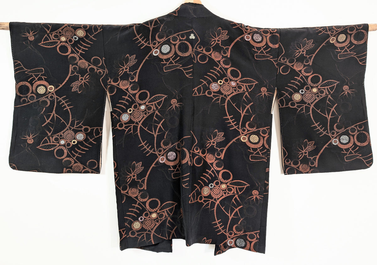 Vue de dos d'une veste kimono japonaise authentique en soie noire, ornée de motifs floraux et de cercles cuivrés aux accents dorés et argentés.
