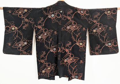 Vue de dos d'une veste kimono japonaise authentique en soie noire, ornée de motifs floraux et de cercles cuivrés aux accents dorés et argentés.