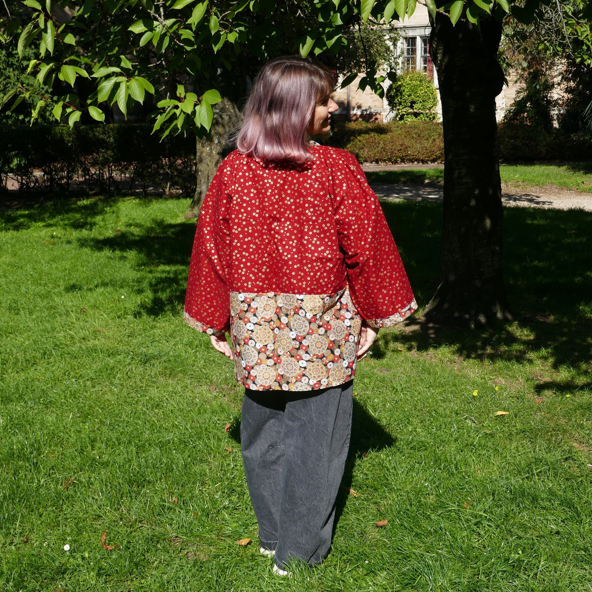 Mikan de dos en veste kimono traditionnelle haori moderne de l'atelier KOGEDO rouge, motif chrysanthèmes 菊 et sakura, dans un parc à Paris.