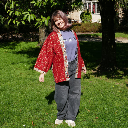 Mikan souriante en veste kimono traditionnelle haori moderne de l'atelier KOGEDO rouge, motif chrysanthèmes 菊 et sakura, dans un parc à Paris.
