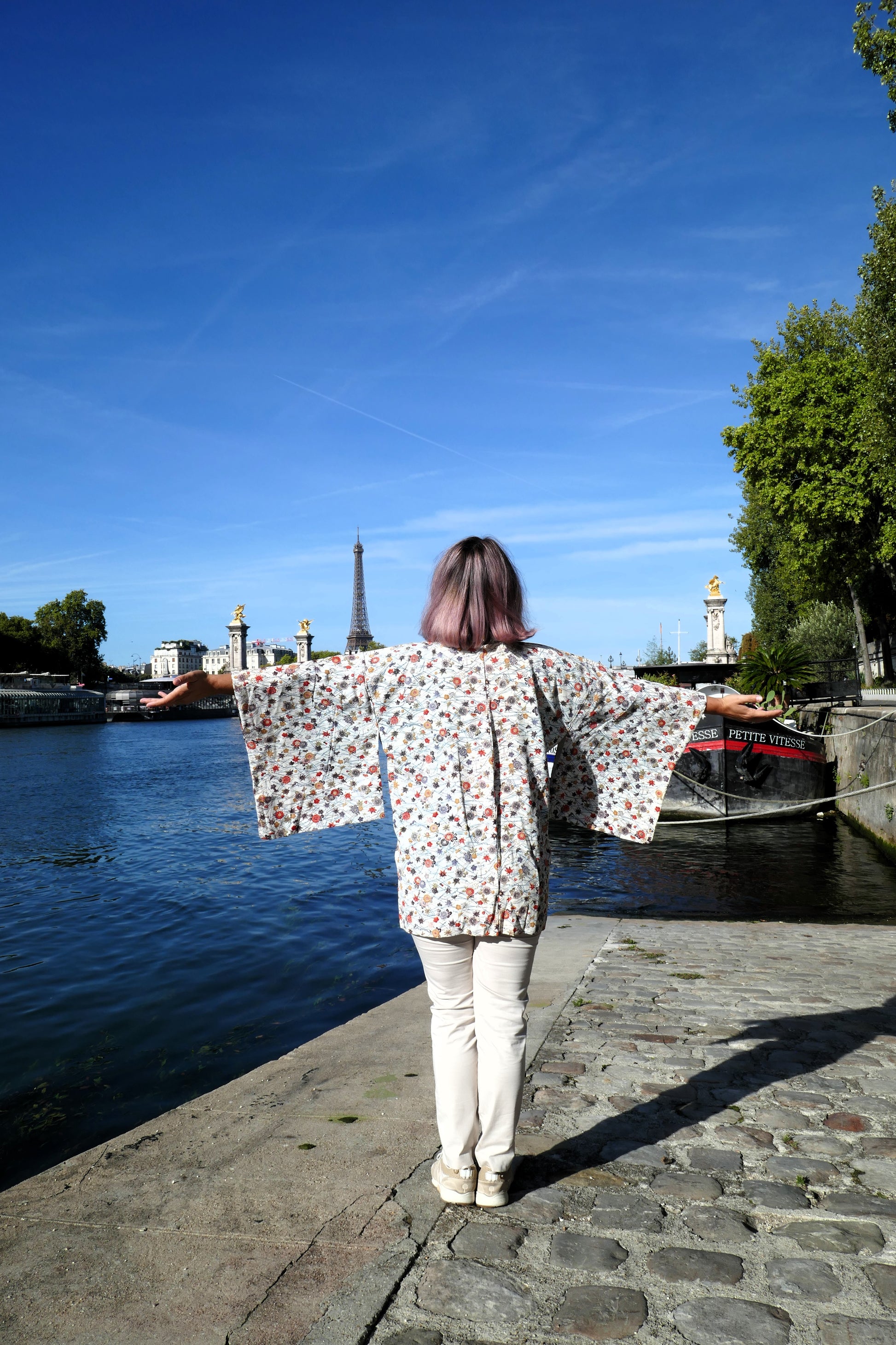Mikan portant une veste kimono traditionnelle haori vintage en soie, motif 菊と紅葉 (kiku et momiji), bras ouverts face à la Seine et la tour Eiffel.