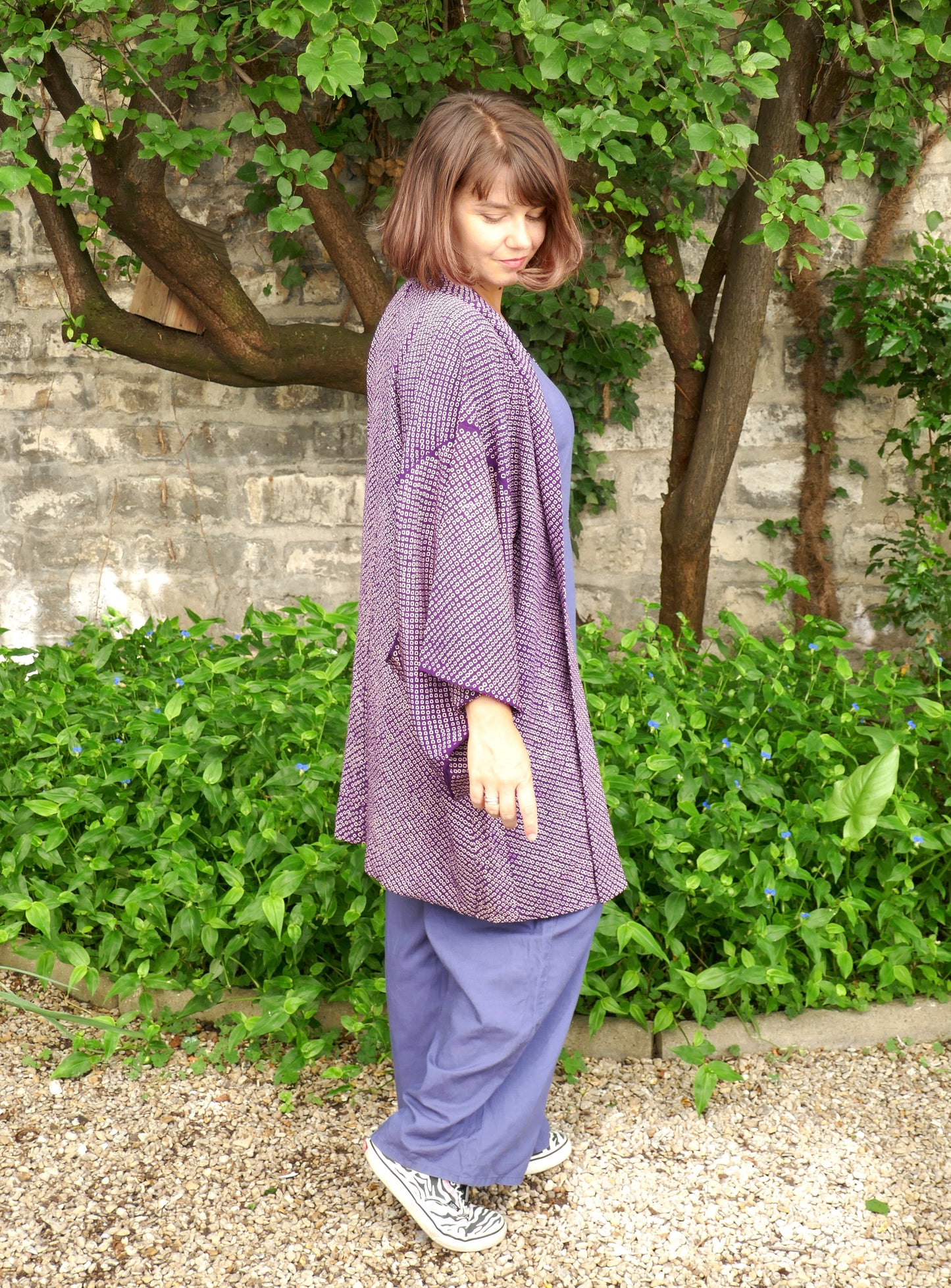 Veste kimono haori vintage violet vue de profil sur une femme, coupe ample et fluide, tissu en soie avec motifs traditionnels japonais shibori, ambiance zen en extérieur.