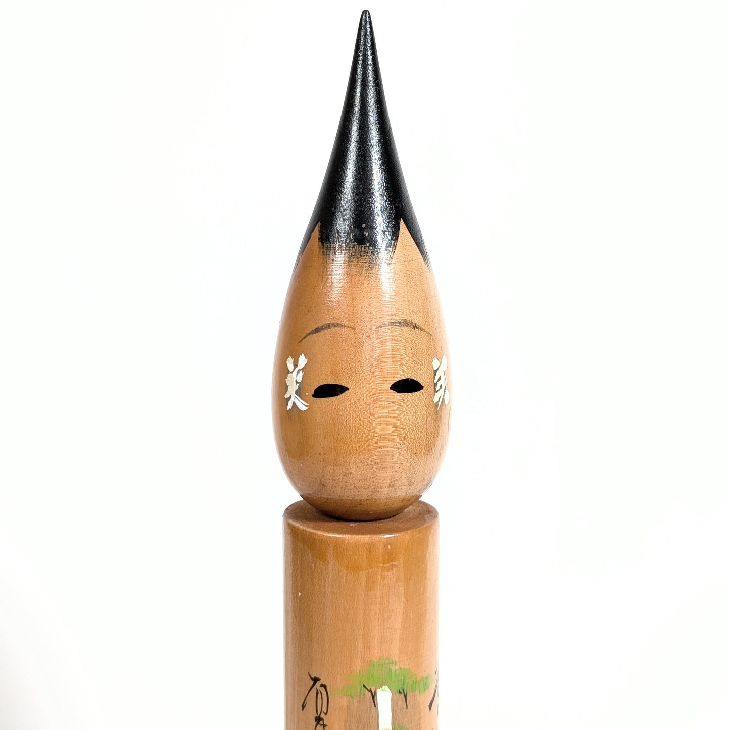 Gros plan du visage d’une fude kokeshi en bois, kanji 美 sur les joues, cheveux noirs laqués