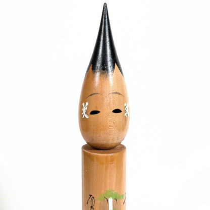 Gros plan du visage d’une fude kokeshi en bois, kanji 美 sur les joues, cheveux noirs laqués