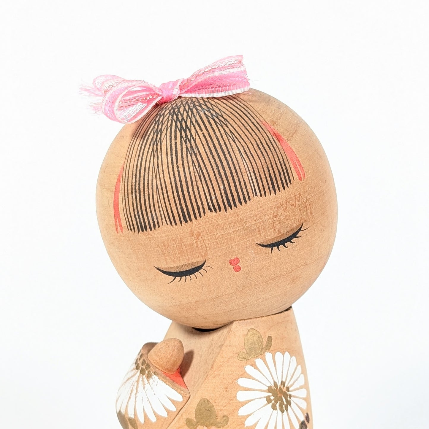 visage kokeshi japonaise cheveux peints frange fine noeud rose expression douce artisanat bois