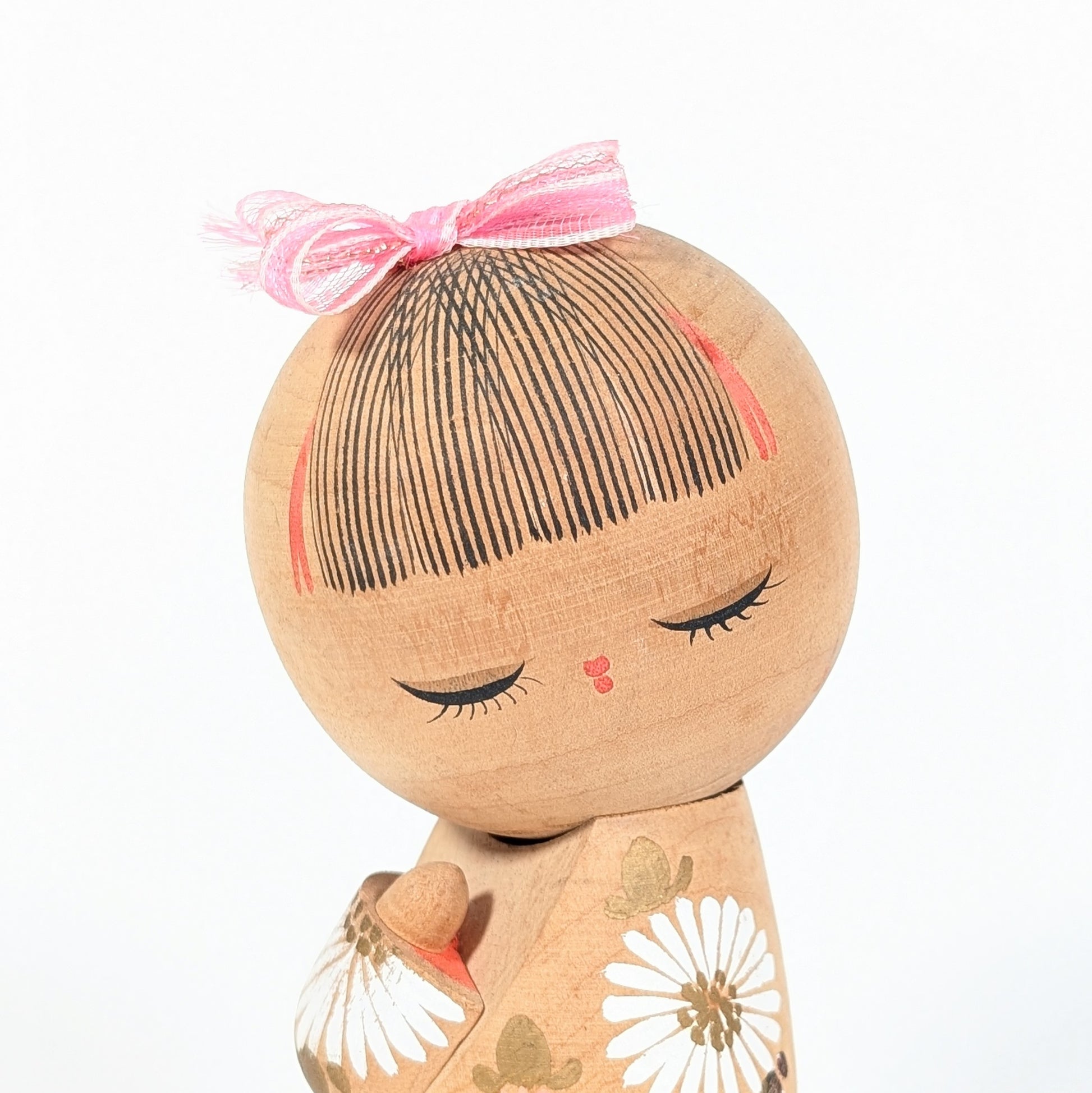 visage kokeshi japonaise cheveux peints frange fine noeud rose expression douce artisanat bois