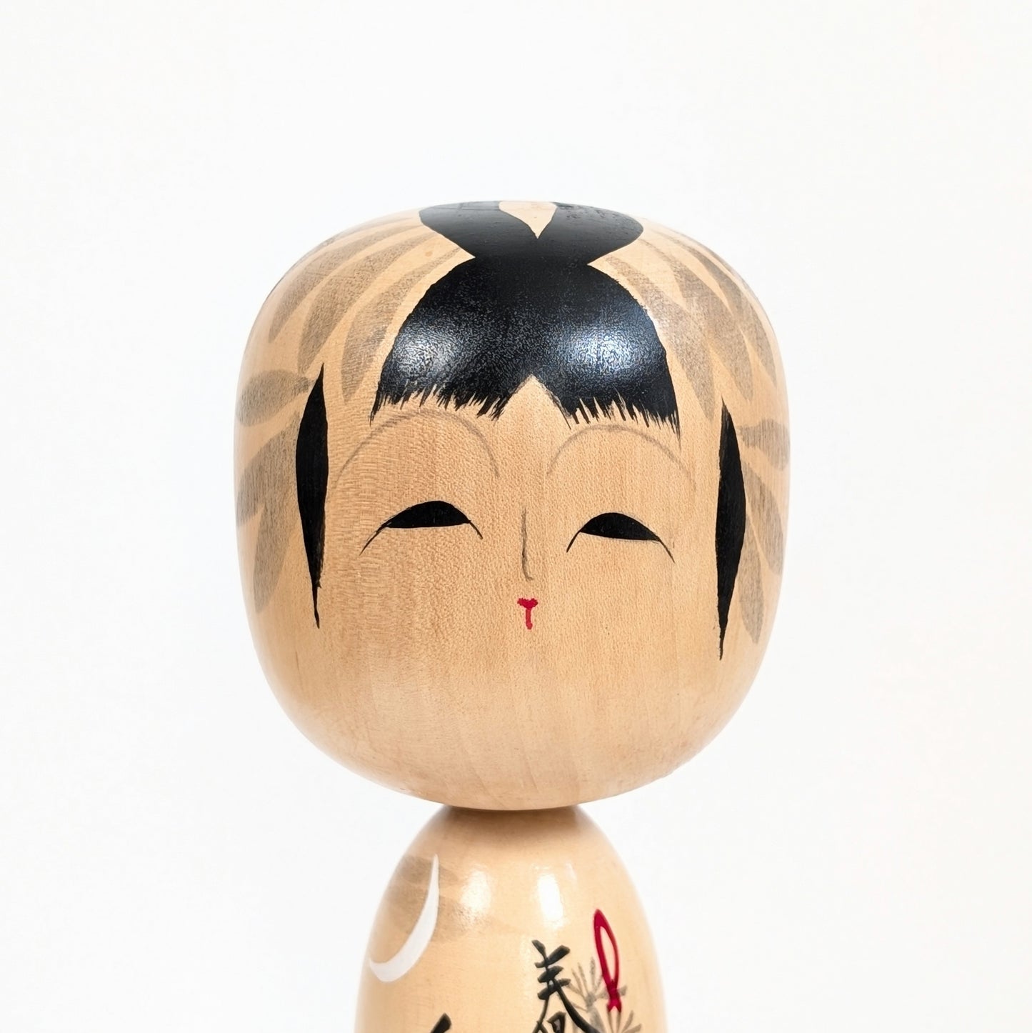 Gros plan sur le visage peint de la kokeshi japonaise Shūhō, coiffure noire et traits traditionnels stylisés.