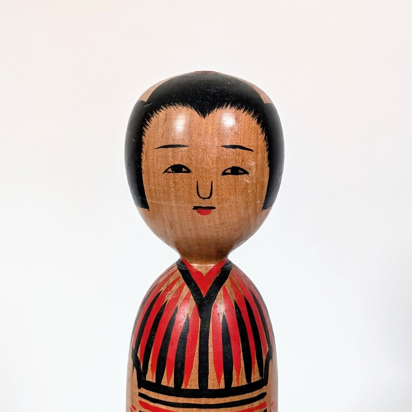 Visage peint d’une kokeshi japonaise traditionnelle, expression douce, artisanat japonais ancien