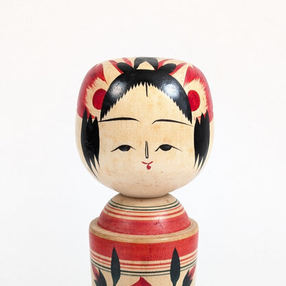 Détail du visage d’une kokeshi Naruko de Suzuki Toshiyuki, fils de Unkichi avec yeux hitoemabuta 一重瞼, coiffure noire et ornements rouges traditionnels.