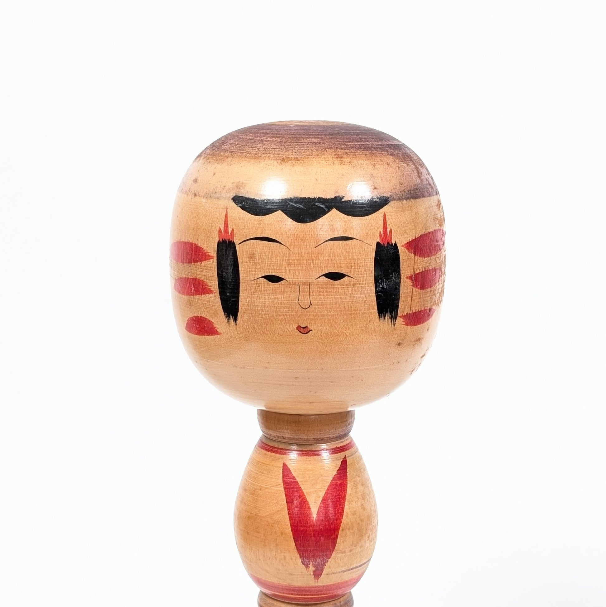 Détail du visage peint d’une kokeshi Ogura Katsushi, avec coiffure noire, ornements rouges et grain naturel du bois