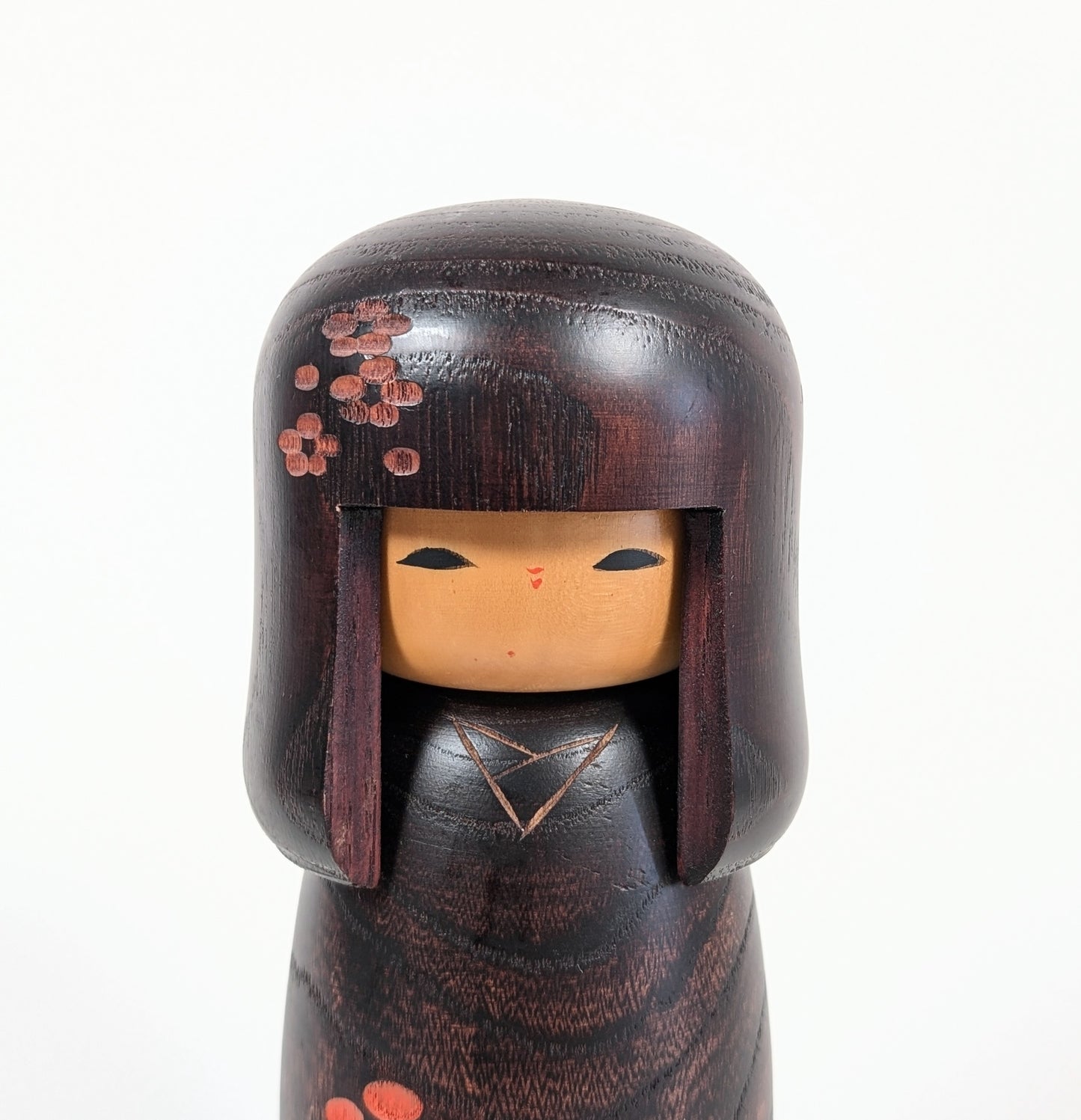 Gros plan du visage d’une kokeshi Usaburo Shunsai, coiffure okappa et fleurs ume