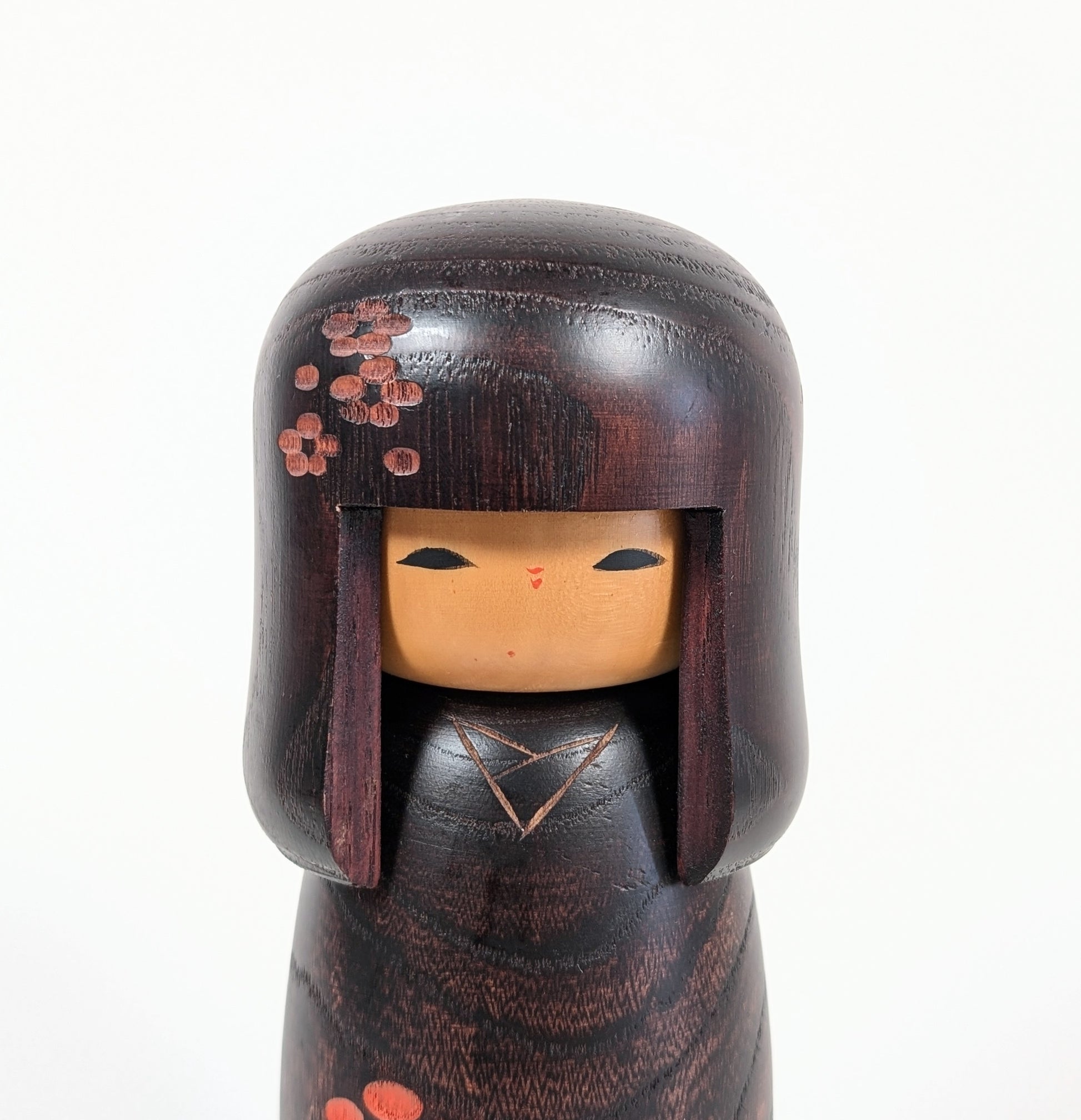 Gros plan du visage d’une kokeshi Usaburo Shunsai, coiffure okappa et fleurs ume