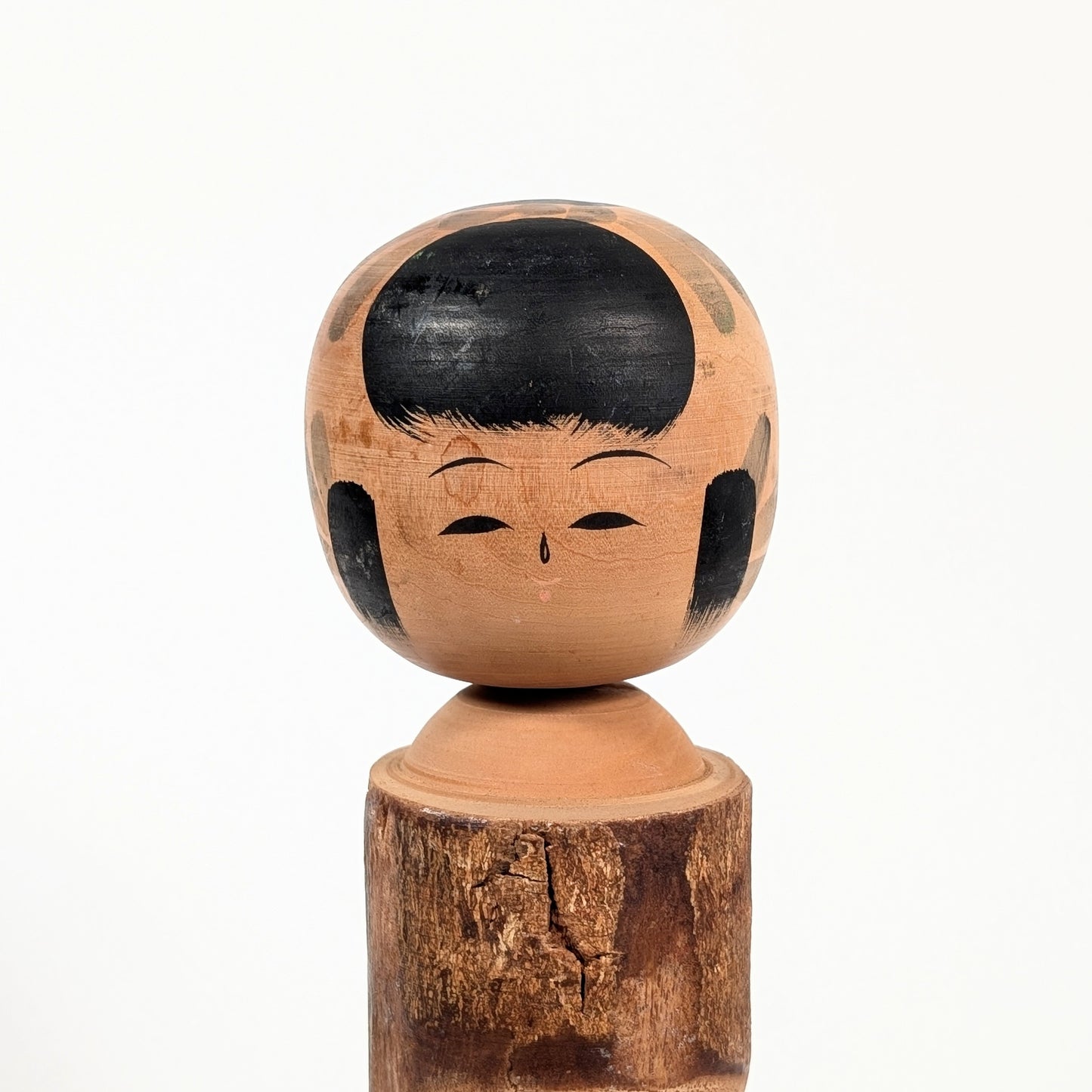 Détail du visage doux d’une kokeshi omiyage signée Kômura 香村, coiffure noire okappa et expression traditionnelle japonaise.