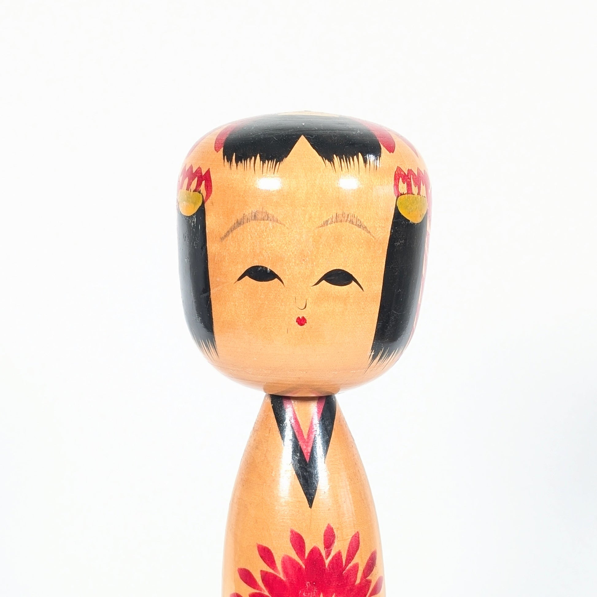 Détail du visage shingata d’une kokeshi japonaise Ryosaku, avec coiffure noire, fleurs kiku et touches jaunes dans les cheveux.