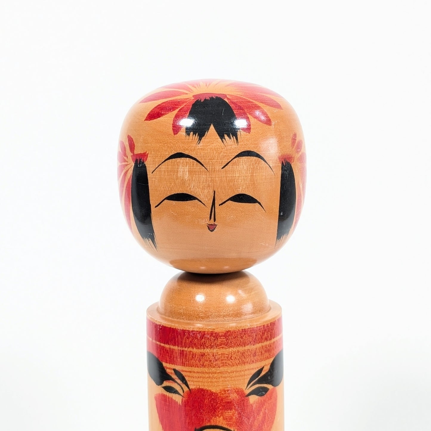 Visage souriant d’une kokeshi shingata Takeshi 武志 avec fleurs de camélia japonais tsubaki 椿