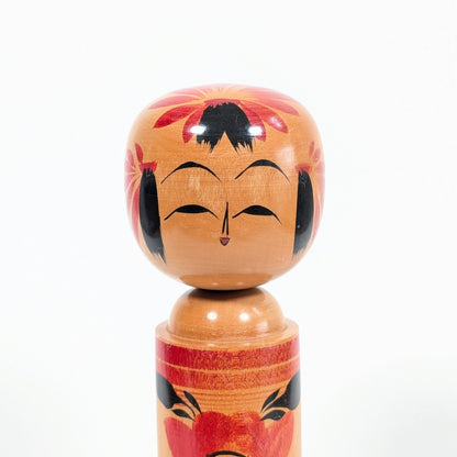 Visage souriant d’une kokeshi shingata Takeshi 武志 avec fleurs de camélia japonais tsubaki 椿