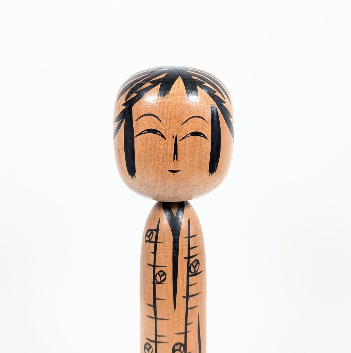 Portrait d'une kokeshi Tōgatta signée Satō Yoshiaki, avec nez ware-bana, yeux à double paupière et expression souriante.