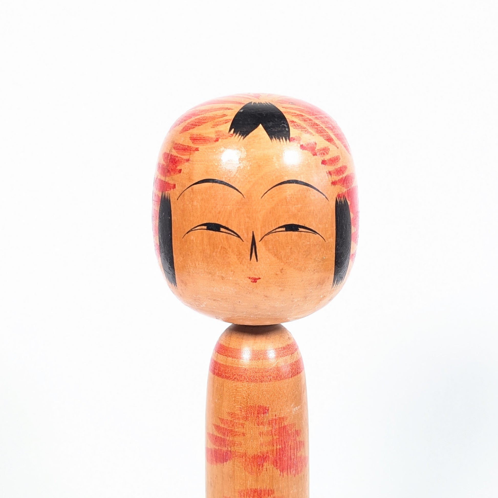 Détail du visage d’une kokeshi Togatta par Onuma Shoji, yeux fins, nez fendu, mèches noires et motif tegara rouge sur la tête.