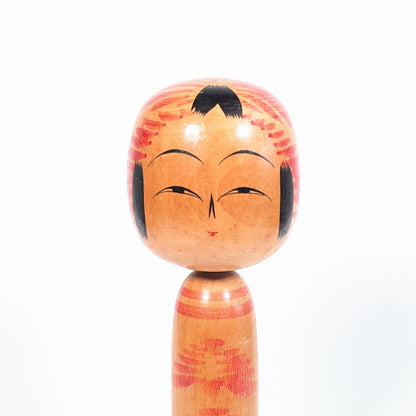 Détail du visage d’une kokeshi Togatta par Onuma Shoji, yeux fins, nez fendu, mèches noires et motif tegara rouge sur la tête.
