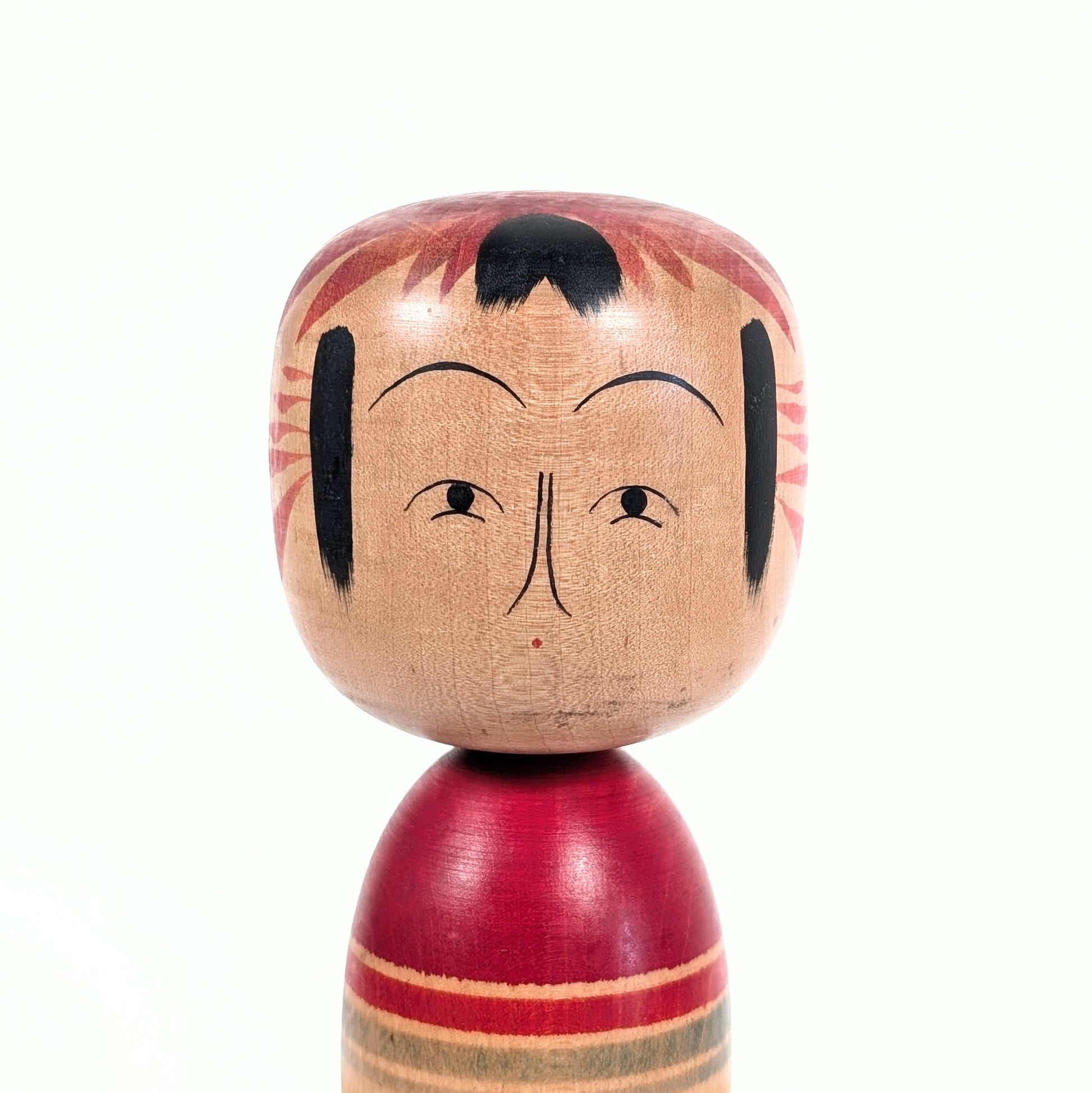 Détail du visage d’une kokeshi Zao Kimura Yusuke, tête arrondie et coiffure rouge et noire typique
