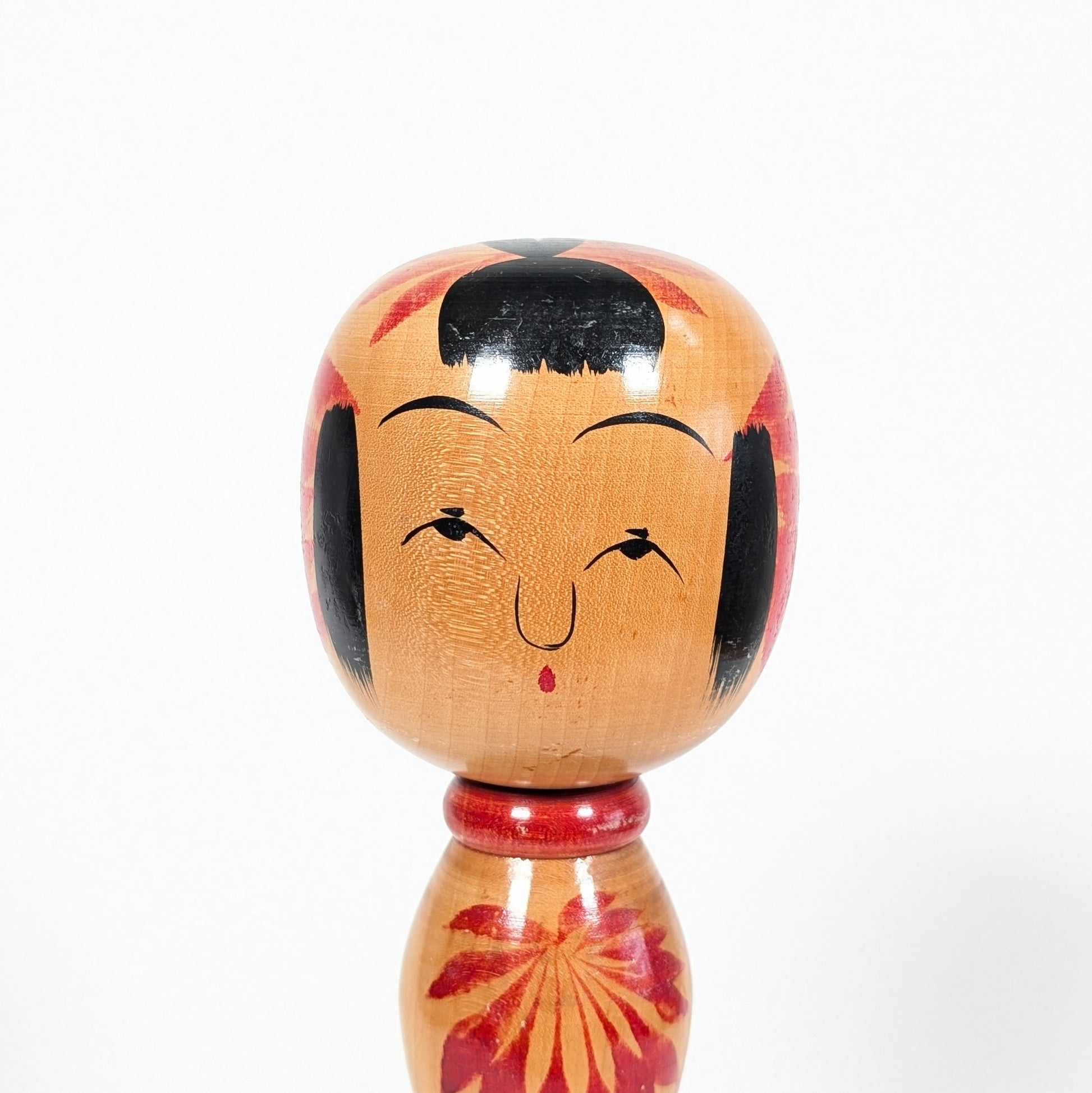 Gros plan du visage d’une poupée kokeshi Yajirō par Hachihoya Kunio, expression souriante, frange noire et peinture artisanale sur bois