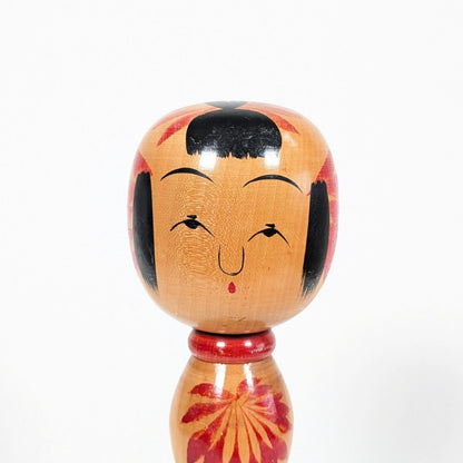 Gros plan du visage d’une poupée kokeshi Yajirō par Hachihoya Kunio, expression souriante, frange noire et peinture artisanale sur bois