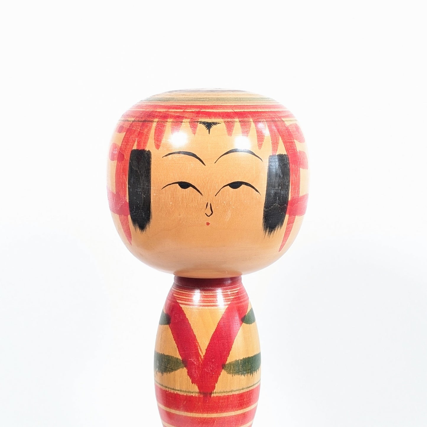 Visage d’une kokeshi Yajirō par Niiyama Hisashirō, grande tête ronde, yeux mi-clos, frange rouge et expression douce typique des dentō kokeshi